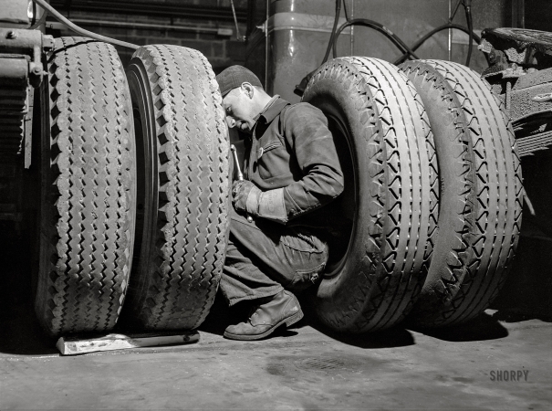 Photo showing: Air Man -- March 1943. Baltimore, Maryland. Davidson Transfer Company trucking terminal. Checking the tires on truck tractors.